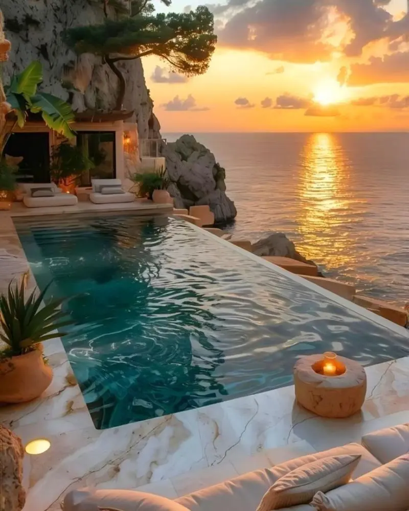 Piscina infinita en terraza sobre acantilado frente al mar con atardecer dorado